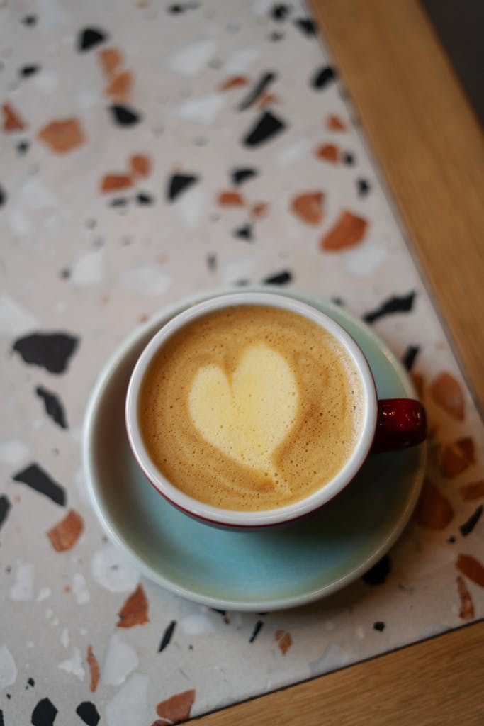 A delicious cappuccino with heart-shaped foam art served in a ceramic cup on wood table.